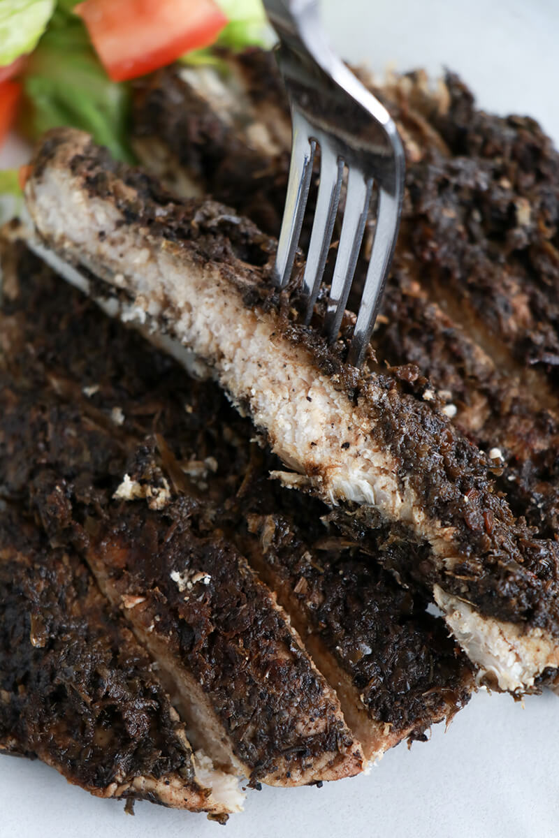 Close-up of juicy sliced jerk chicken with fork and side salad.