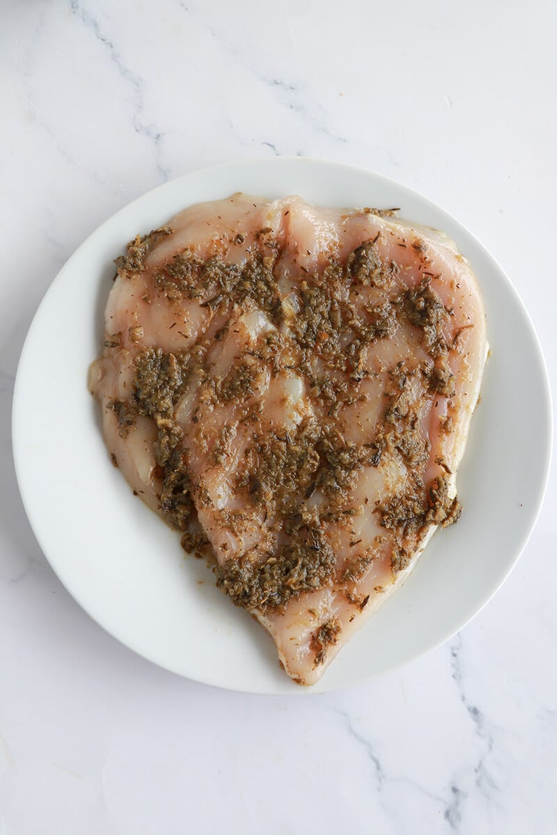 Chicken breast coated in green seasoning marinade, ready for cooking.