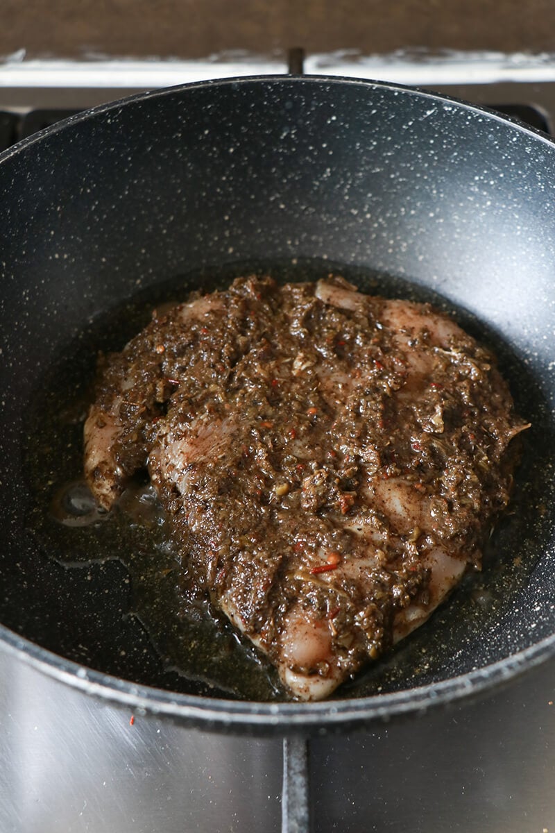 Marinated jerk chicken breast cooking in a skillet on the stove top.
