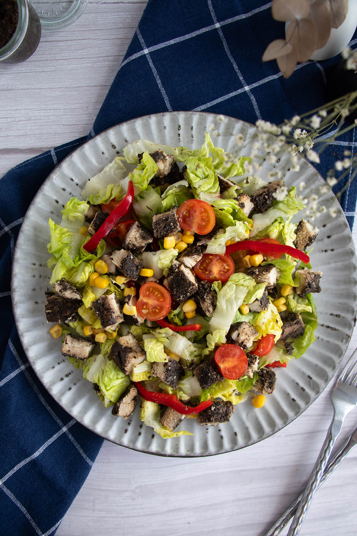 Overhead view of jerk chicken salad with cherry tomatoes, corn, and romaine on a ceramic plate.