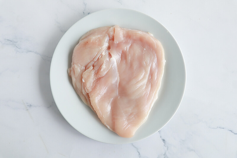 Raw butterflied chicken breast on a white plate, ready to be seasoned.