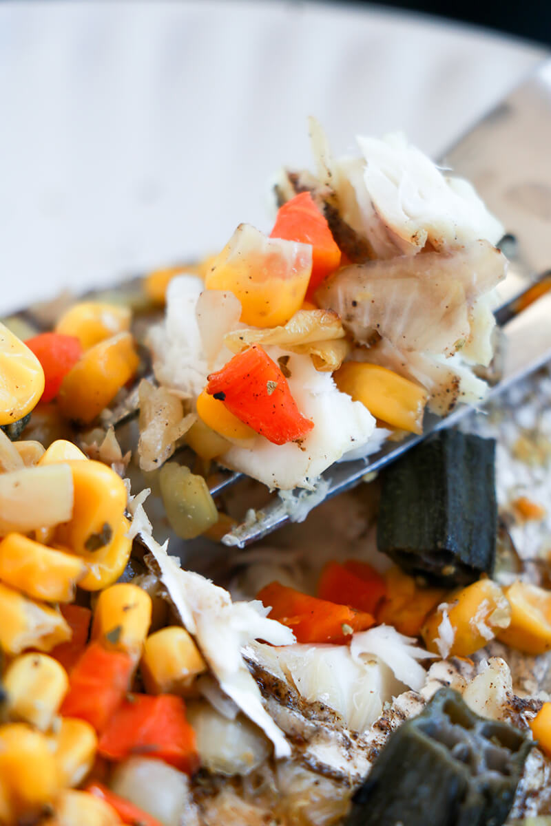 Close-up of a forkful of flaky fish with okra, corn, and carrots from Caribbean-style stuffed fish.