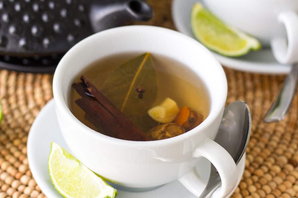 A cup of homemade Caribbean bush tea made with bay leaf, ginger, garlic, cloves, cinnamon, and turmeric.