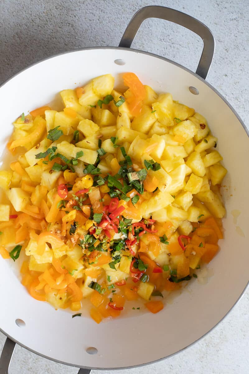 Fresh diced pineapple added to sautéed onions in a pan for pineapple chutney