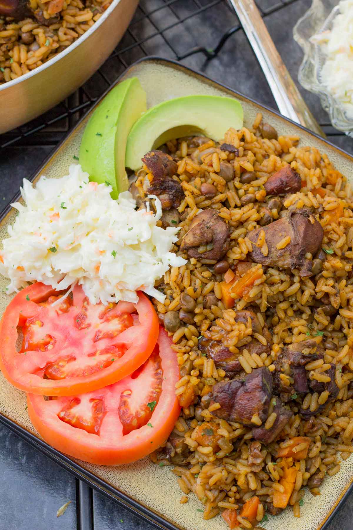 A step by step guide on making the unofficial Trinidad national dish, pelau. A hearty one pot dish of caramelized chicken with rice and pigeon peas. Close-up of Trinidad chicken pelau with coleslaw, tomatoes, and avocado