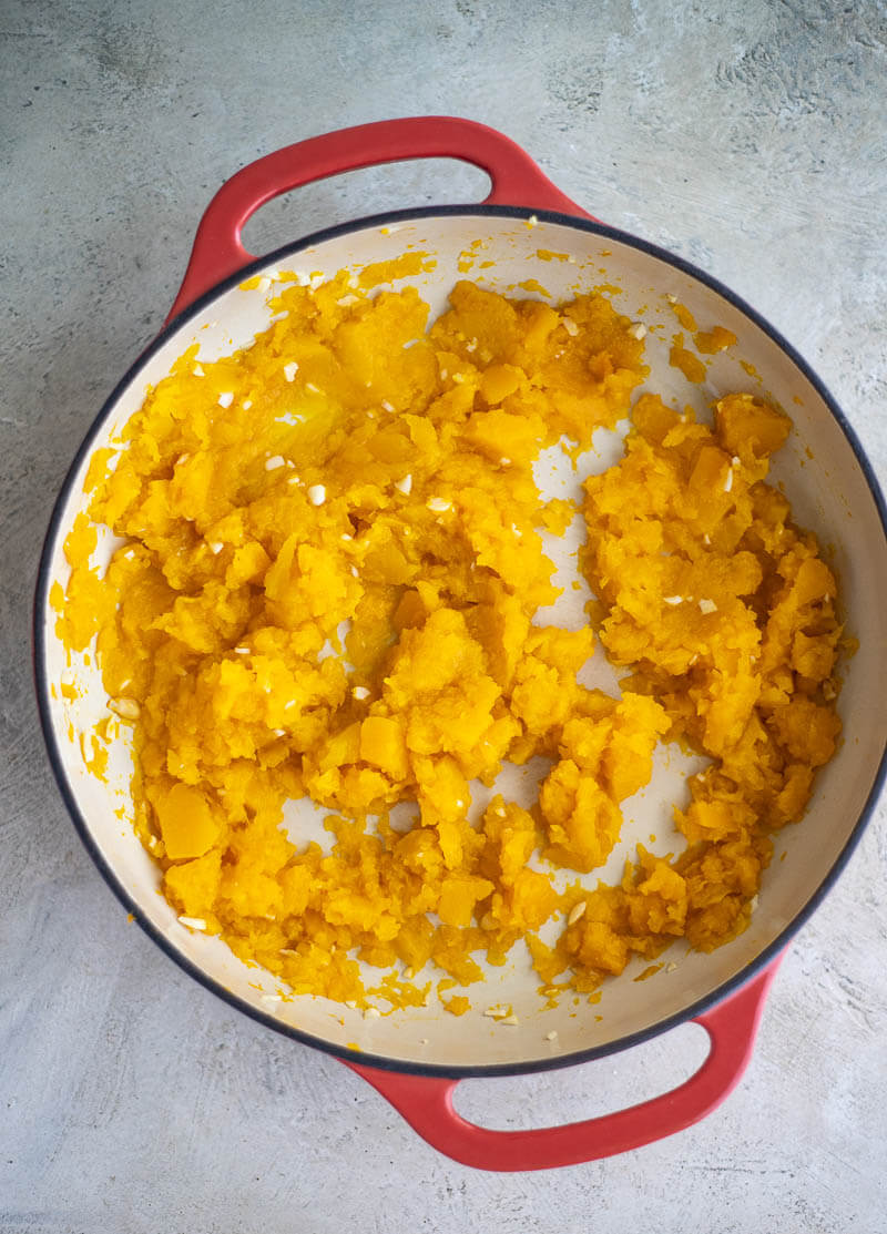 Soft cooked pumpkin being mashed for pumpkin choka
