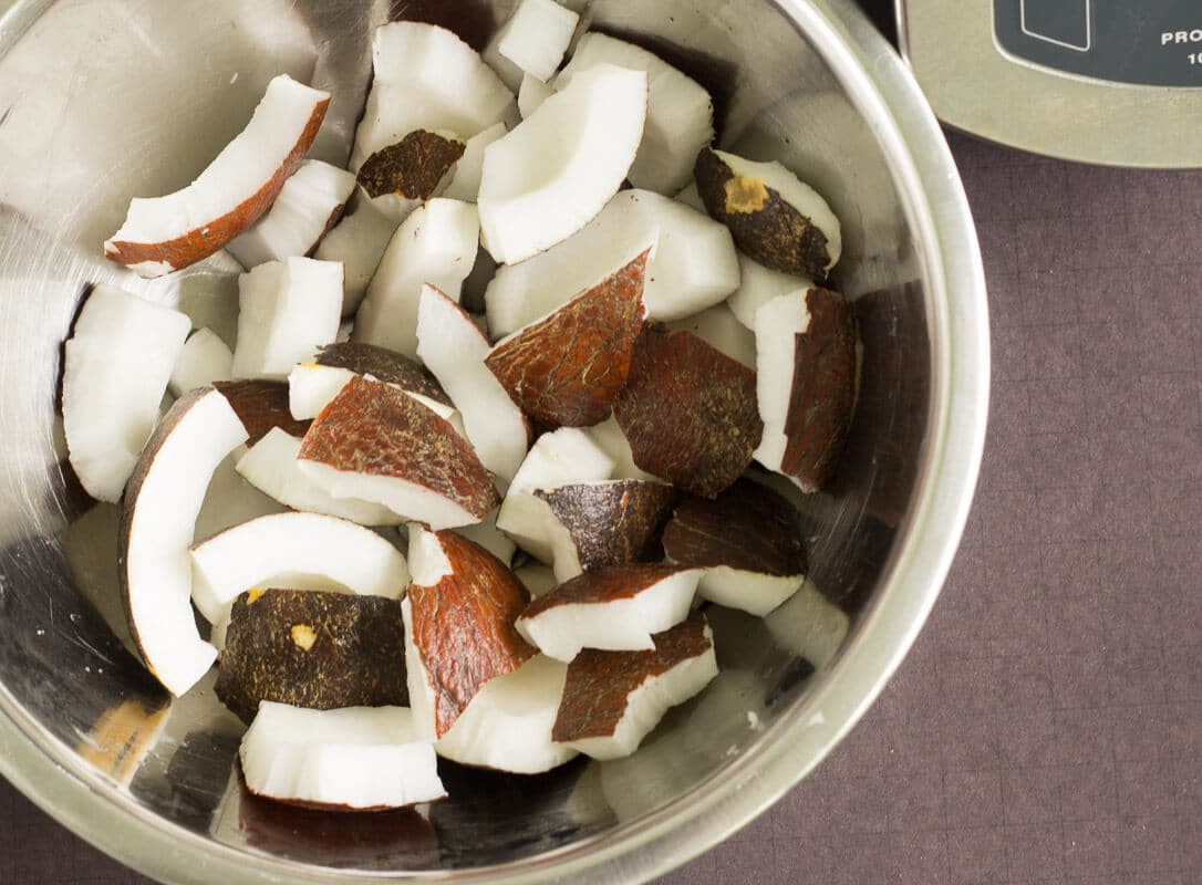 An easy step by step guide for making coconut milk from a fresh dry coconut just like we do it in the Caribbean. Chopped pieces of mature coconut meat in a metal bowl.