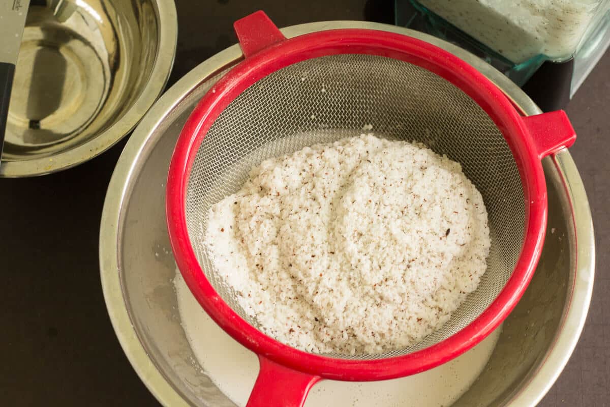 An easy step by step guide for making coconut milk from a fresh dry coconut just like we do it in the Caribbean. Strained coconut pulp resting in a mesh strainer over a bowl.