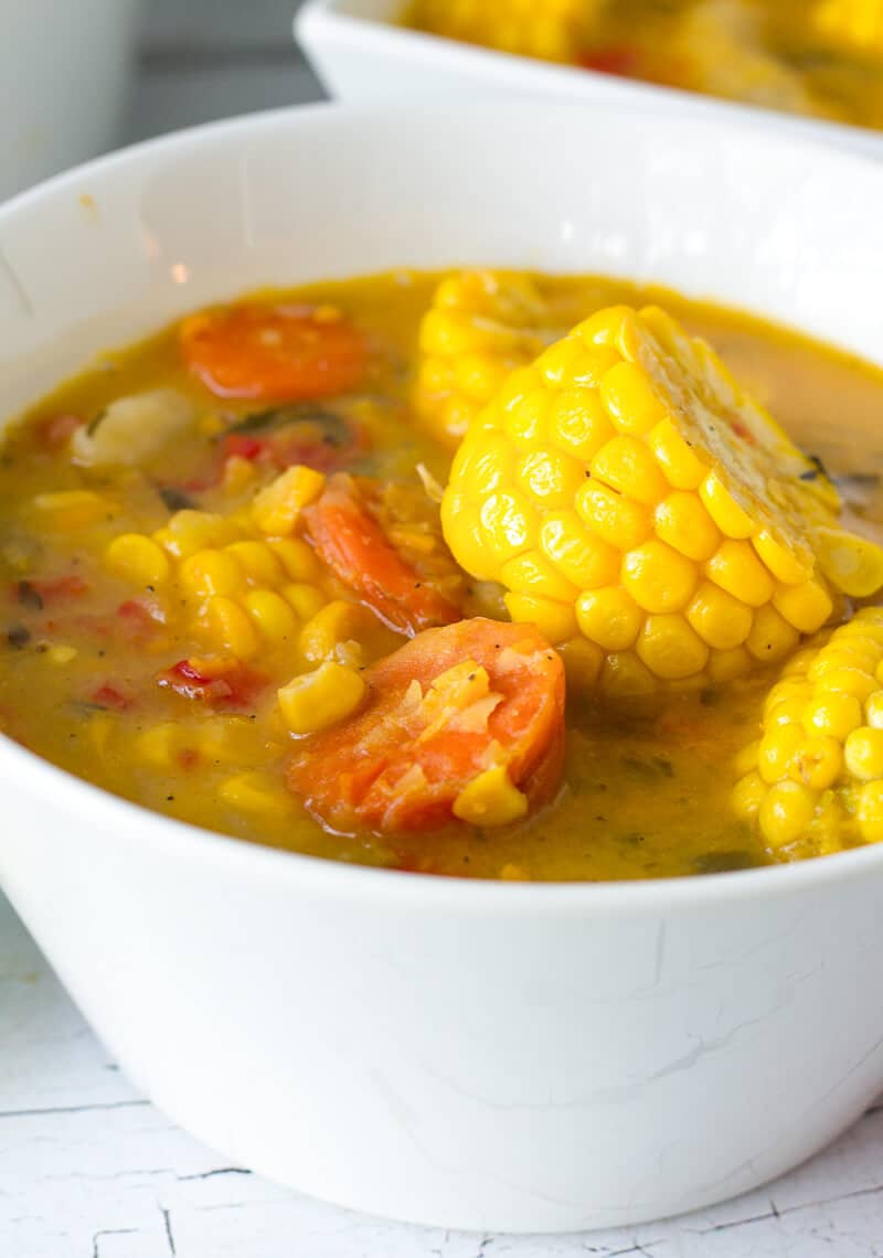 Trinidad corn soup is a popular Trini street food that is ram packed with flavor. from split peas, corn and dumplings. Perfect after fete snack. Close-up of Trinidad and Tobago corn soup in a white bowl with corn discs, carrots, and vegetables in a rich split-pea broth.