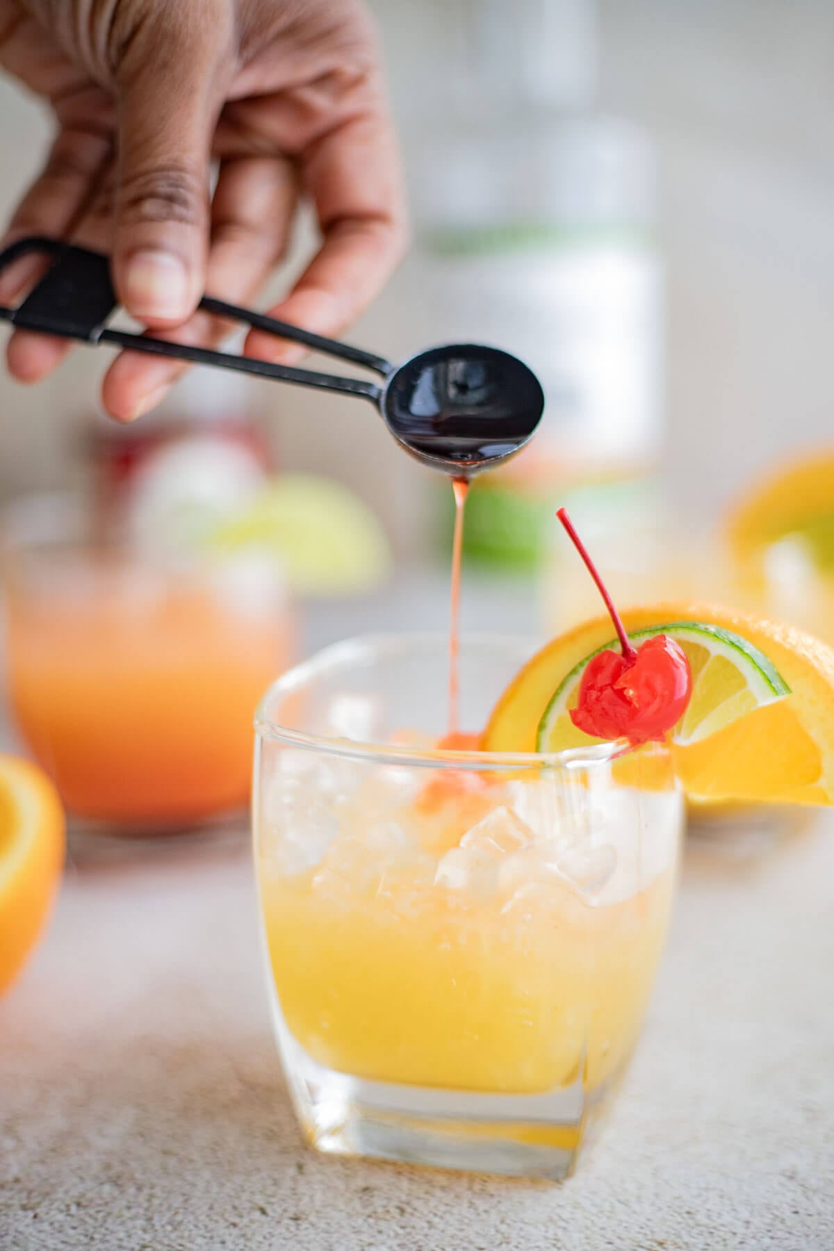 Adding grenadine syrup to a glass of Le Planteur cocktail with citrus garnish.