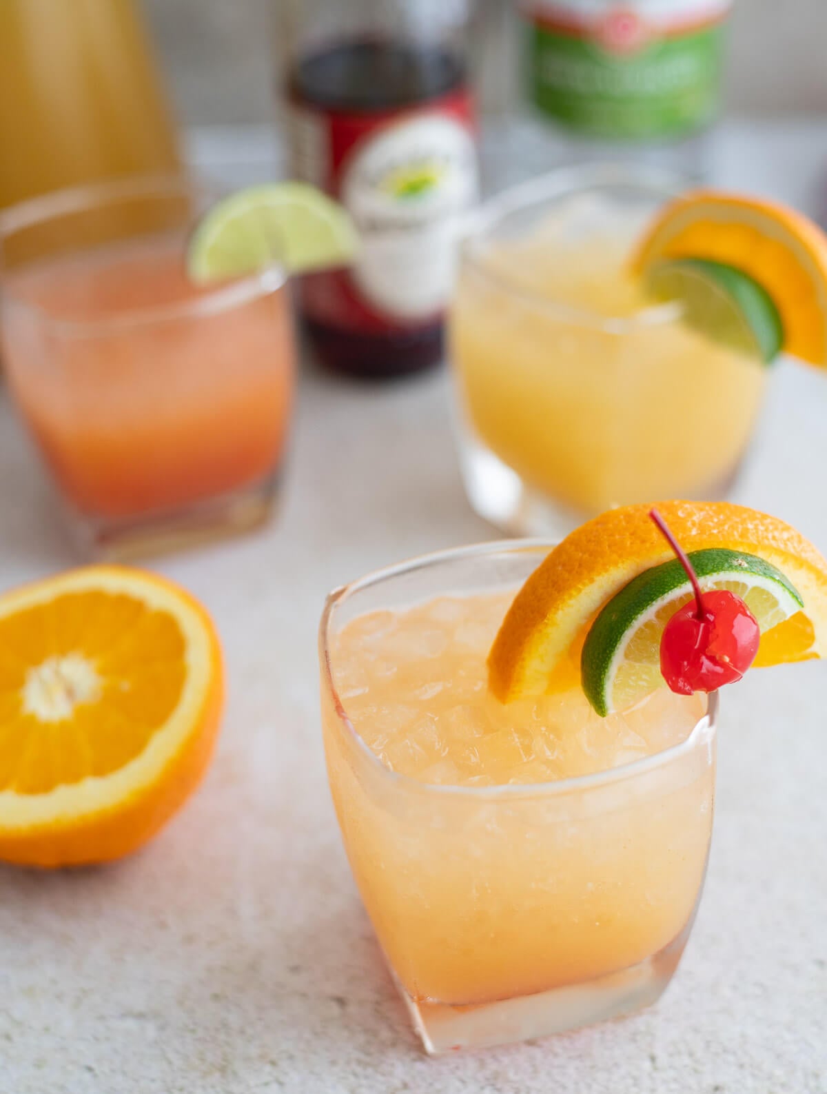 Three glasses of Le Planteur rum cocktail garnished with orange, lime, and a cherry.