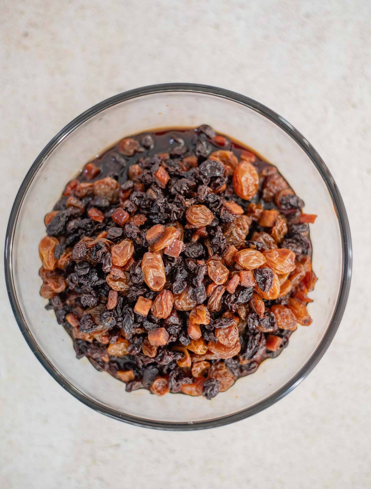 Mixture of dried raisins, sultanas, cherries, and mixed peel soaking in rum in a glass container.