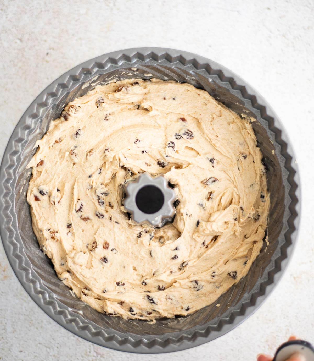 Fruit sponge cake batter with rum-soaked dried fruits spread evenly in a greased Bundt pan before baking.