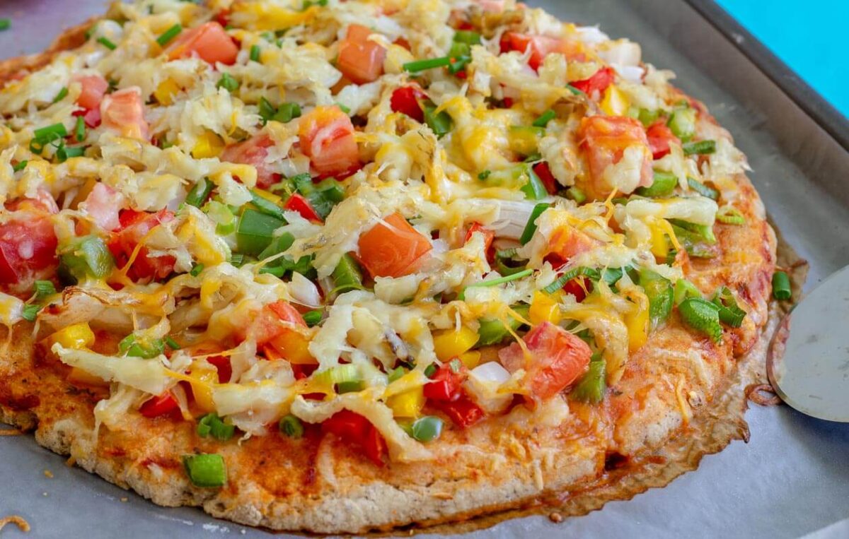 Homemade Caribbean saltfish pizza with fresh vegetables and melted cheese.