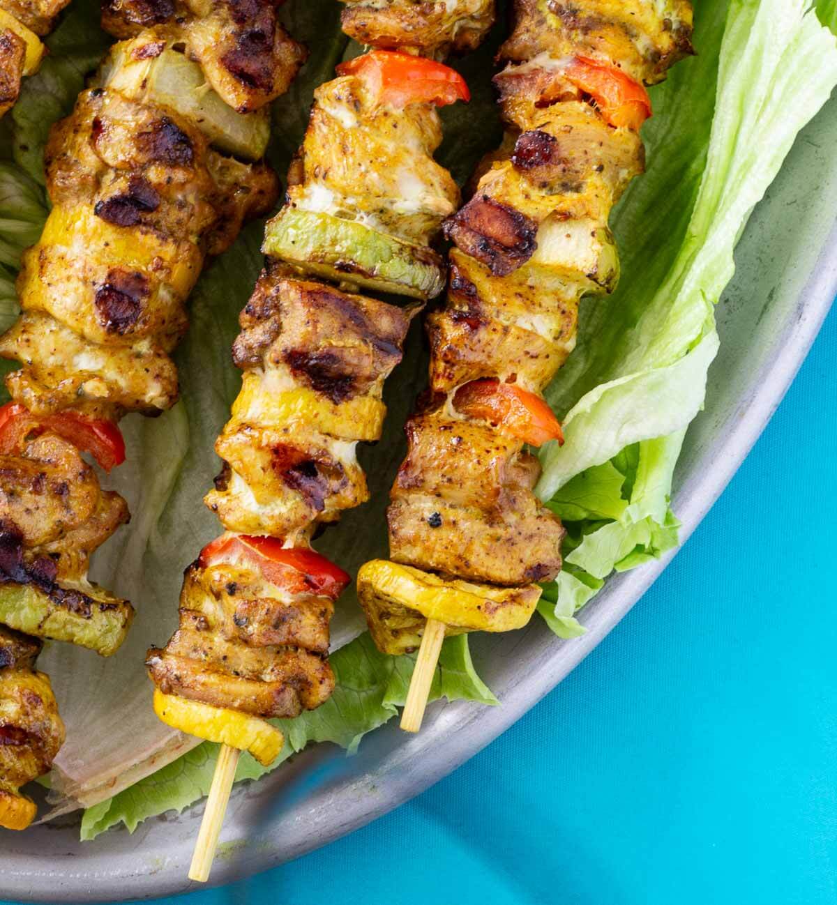 Close-up of grilled Caribbean chicken skewers with golden-brown chicken, christophene, yellow squash, and red bell peppers.