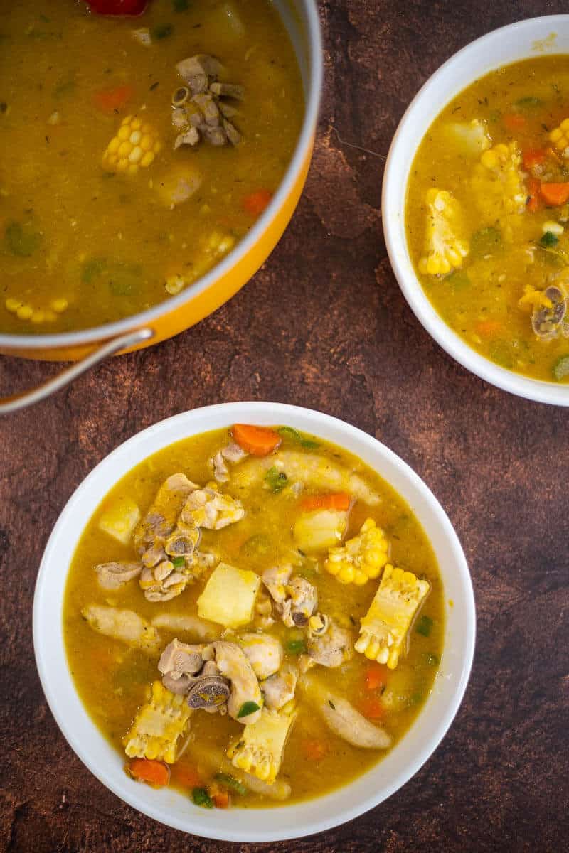 Pot and bowl of Caribbean chicken soup with chicken, corn, vegetables and dumplings