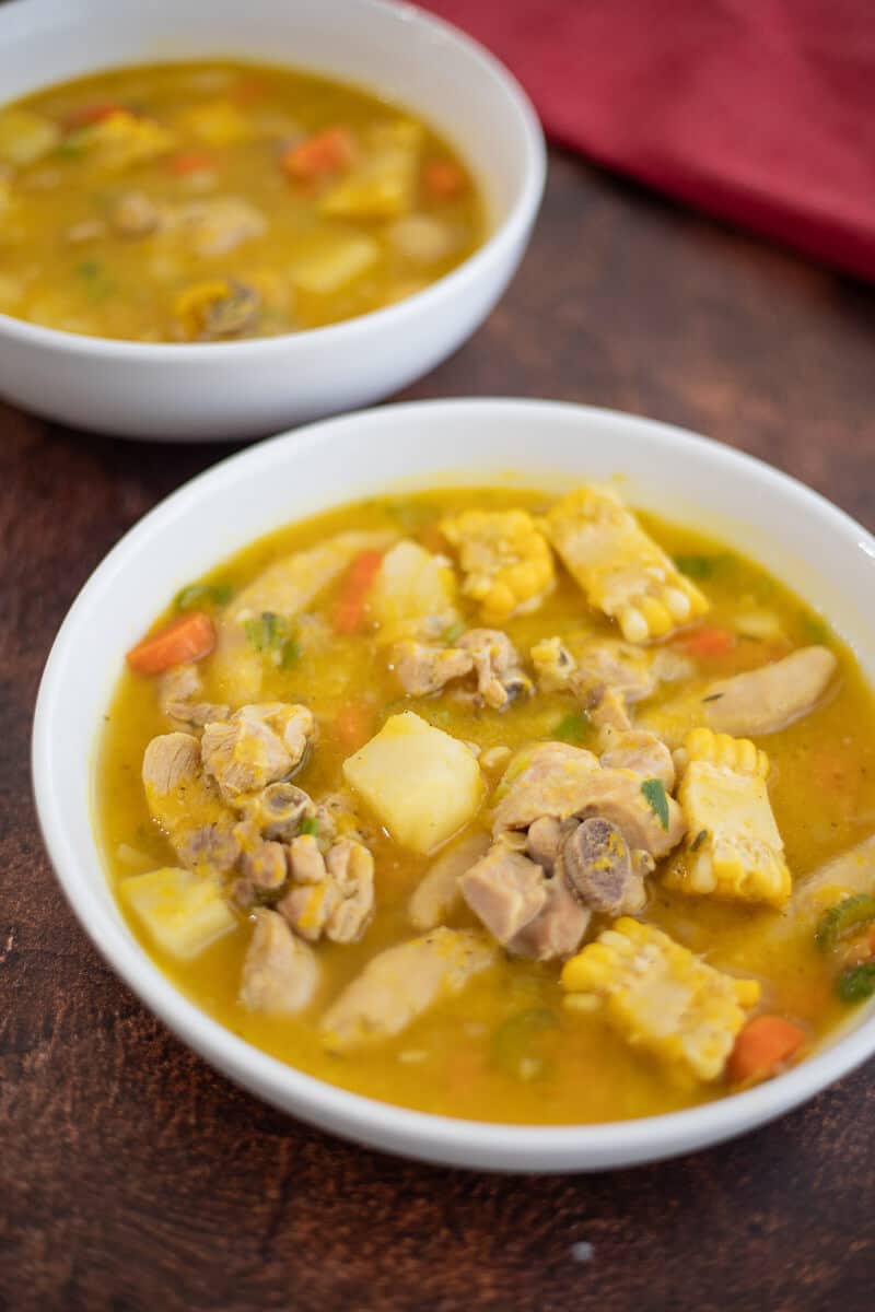 Bowls of Caribbean chicken soup with chicken, corn, potato, carrots and dumplings