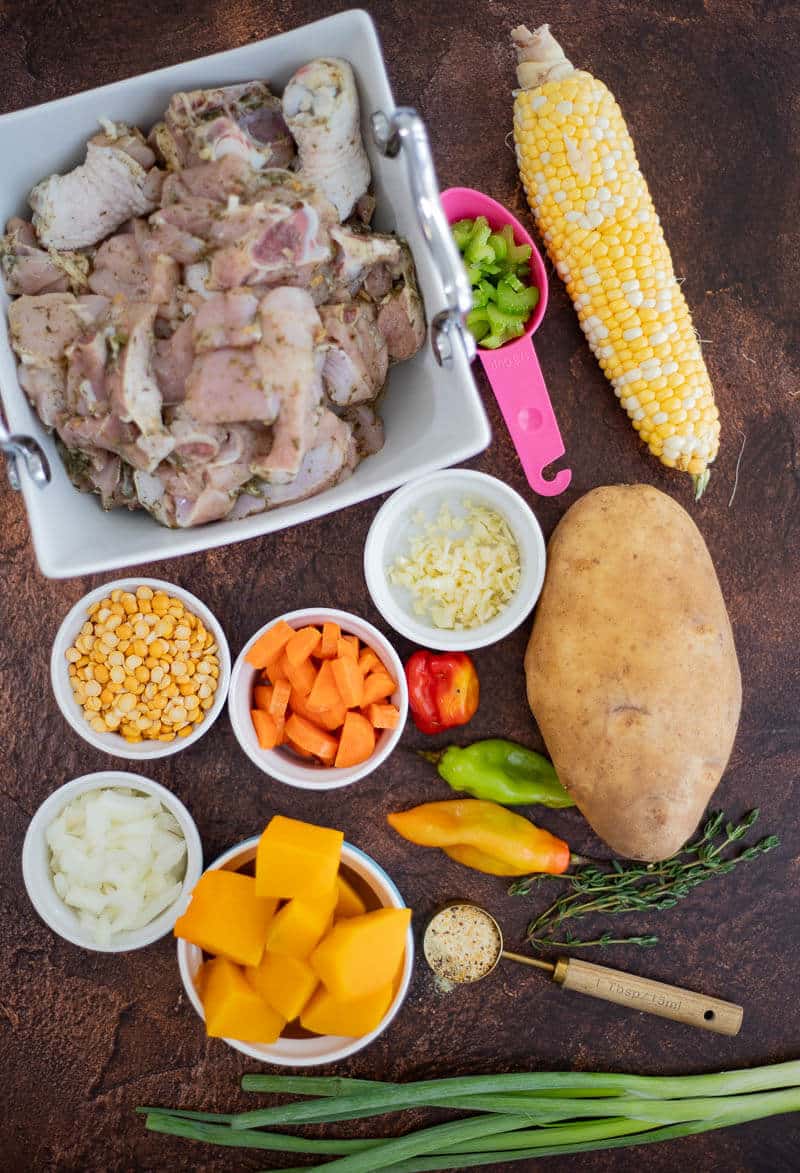 Ingredients for Caribbean chicken soup including seasoned chicken, pumpkin, split peas, potato, corn, carrots and fresh herbs.