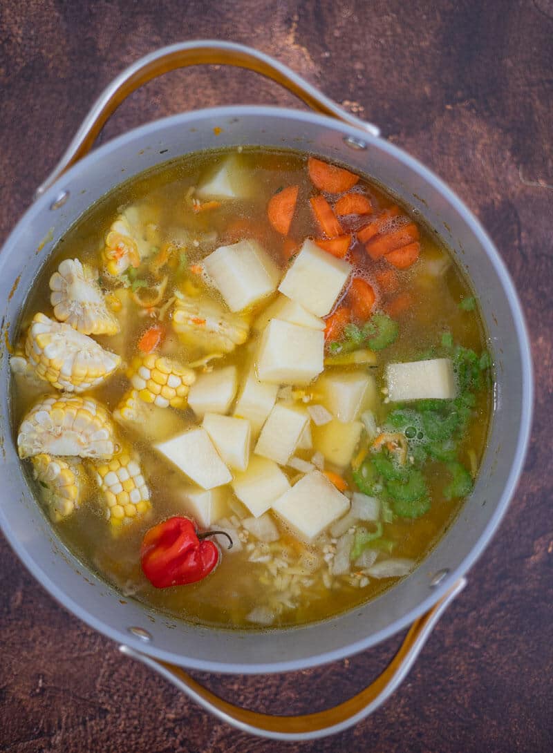 Corn, potatoes, carrots, celery and a whole hot pepper added to the Caribbean chicken soup.