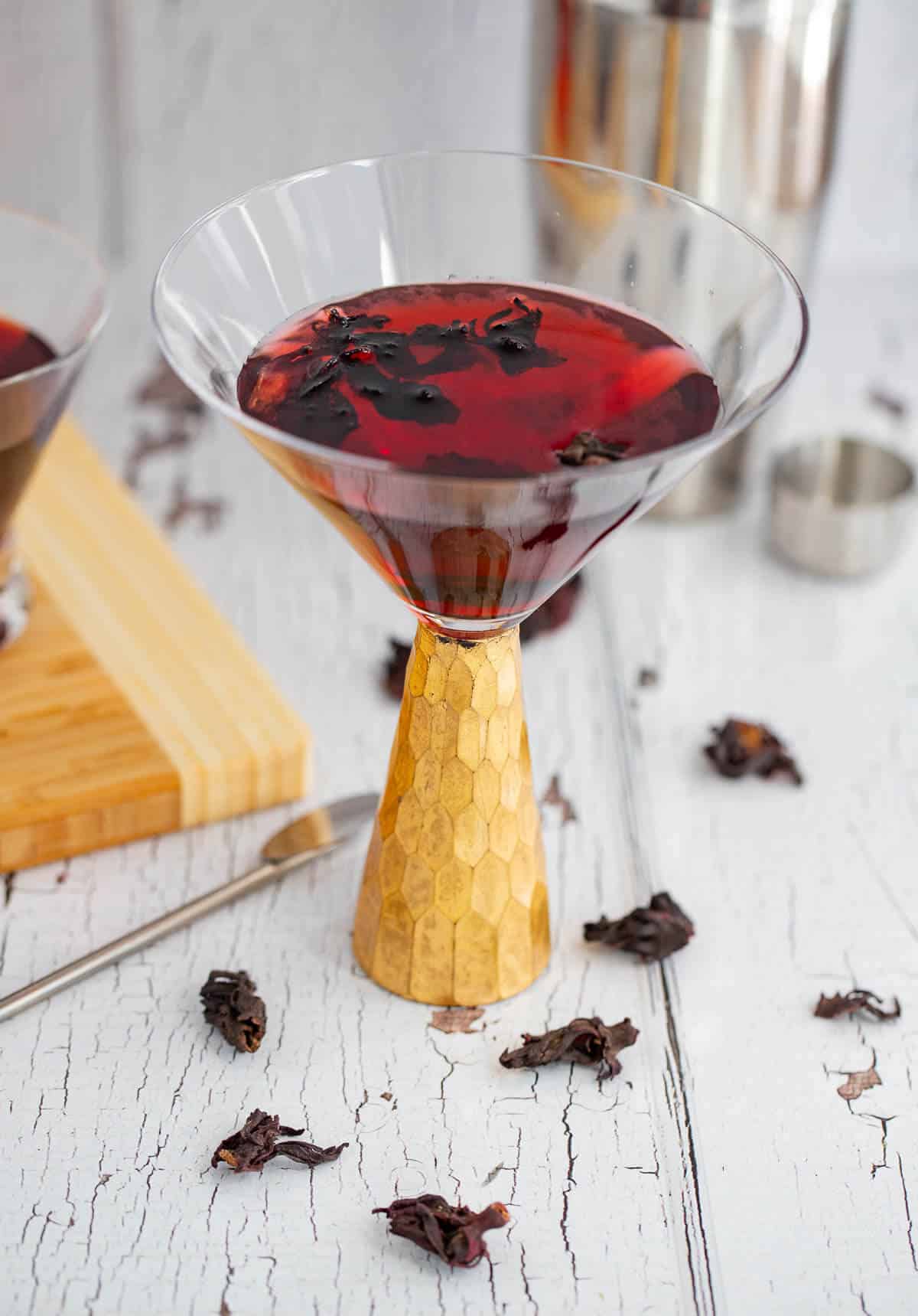 Hibiscus martini made with Caribbean sorrel, gin, Aperol, and ginger syrup in a gold-stemmed cocktail glass.