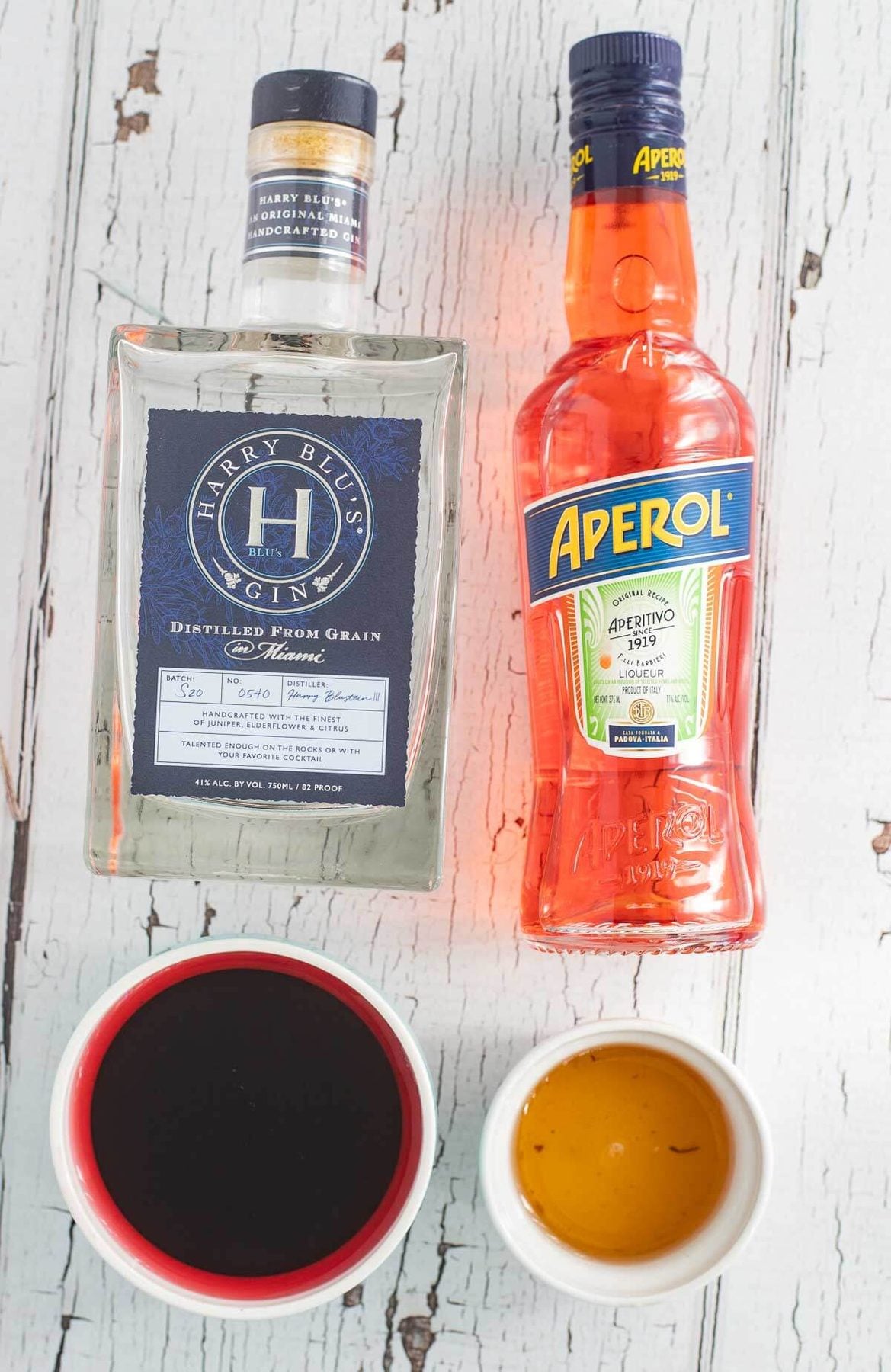 Ingredients for a hibiscus martini, including gin, Aperol, sorrel infusion, and homemade ginger simple syrup.