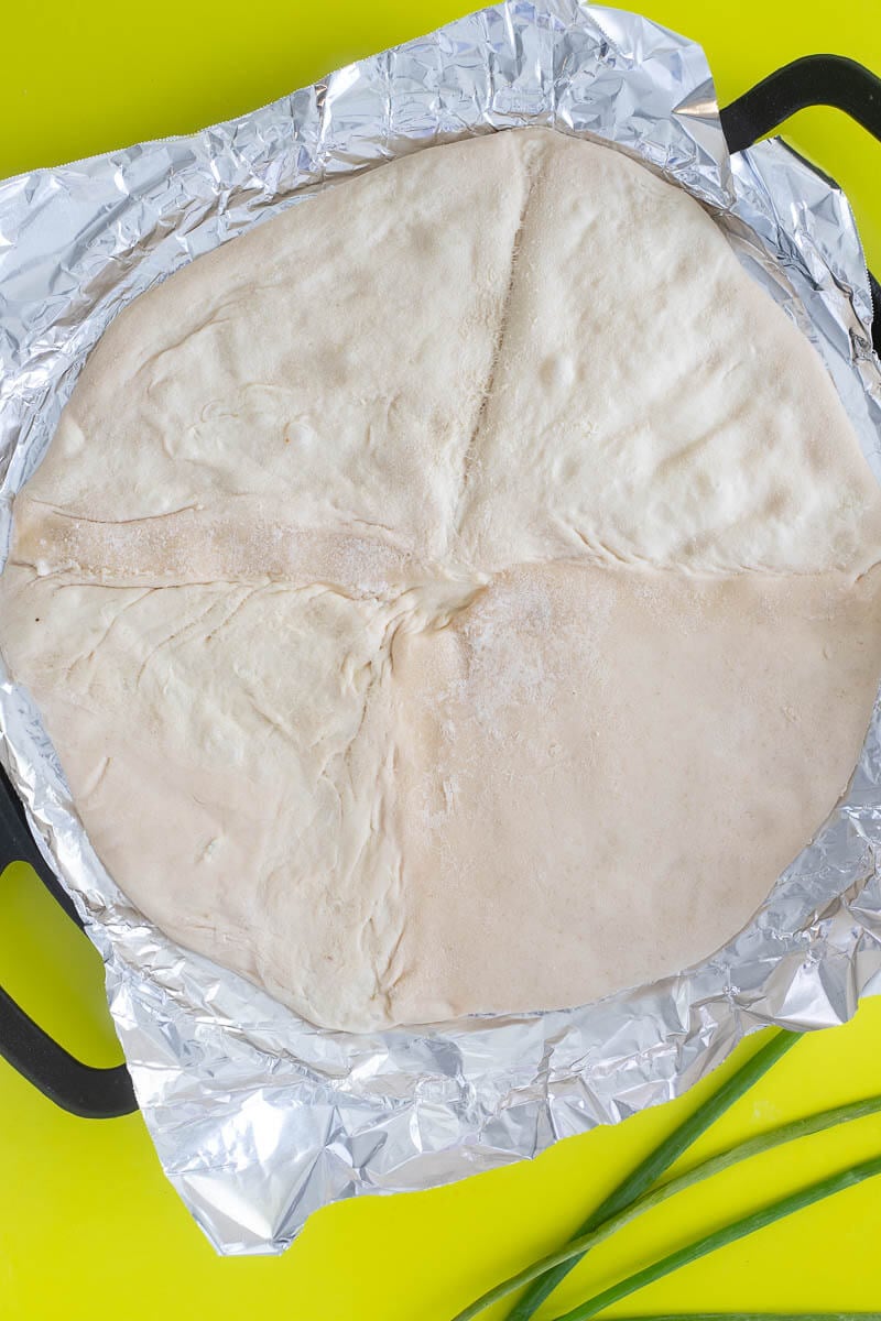 Pizza dough, spread out on a baking stone lined with foil.