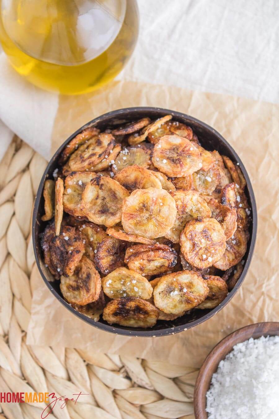 Banana chips in a wooden bowl sprinkled with salt on a wooven basket.