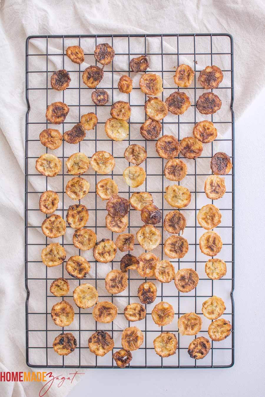Air fried banana chips on a cooling rack on top of a cloth.