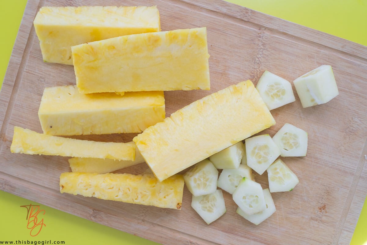Sliced up pineapple, cucumber, on a brown cutting board,