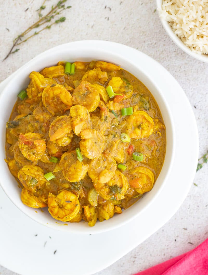 A white bowl full of curry shrimp on a cream background with a pink throw cloth.