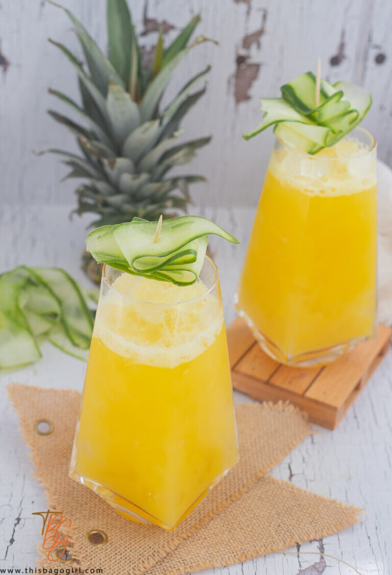 A full glass of pineapple and cucumber juice over ice, with strips of cucumber.