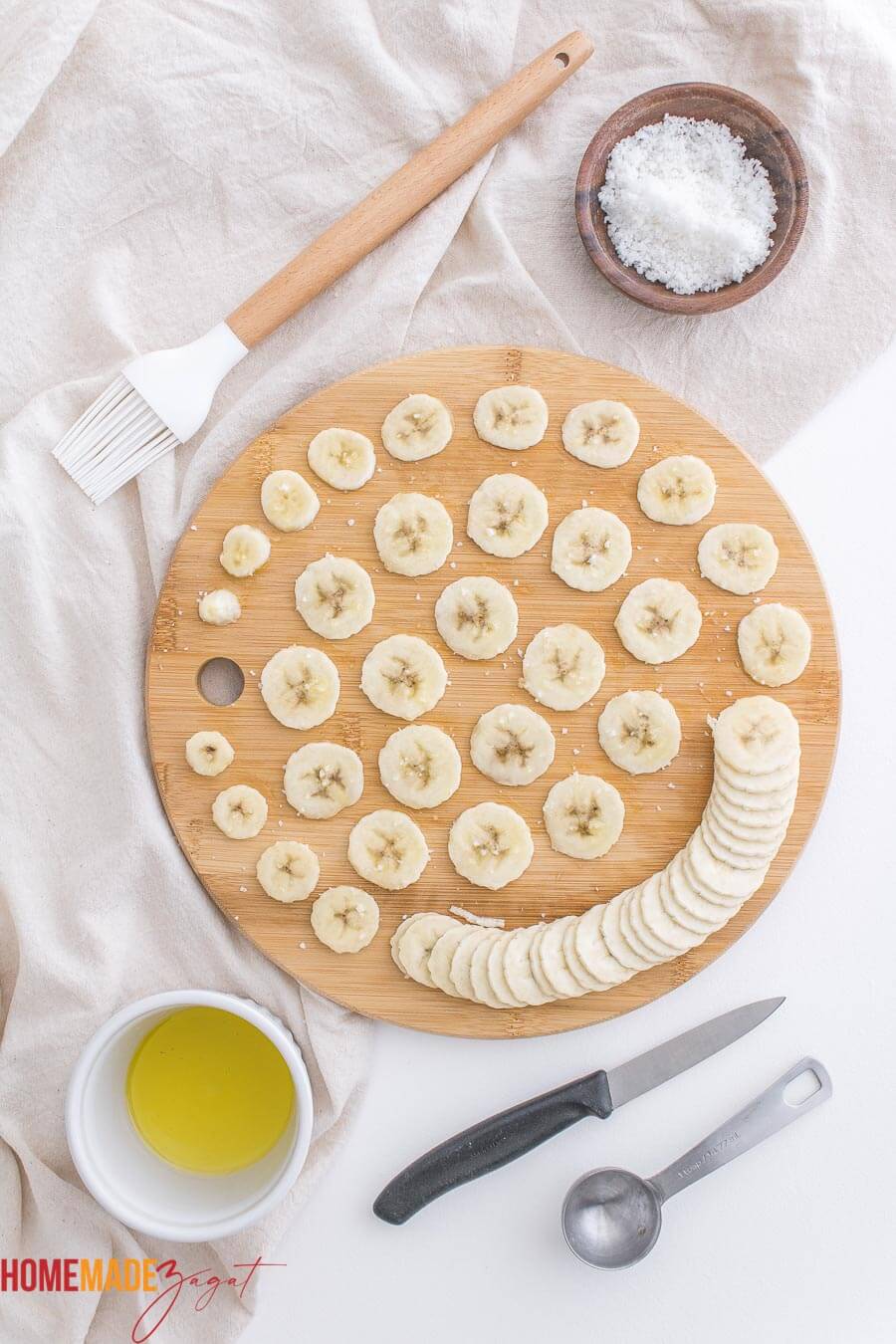 Thinly sliced up bananas with salt sprinkled all over it on a wooden cutting board.