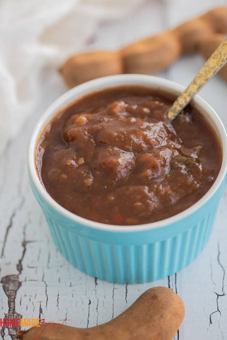 This picture is a blue ramkin filled with tamarind sauce with a few fresh tamarind pods around