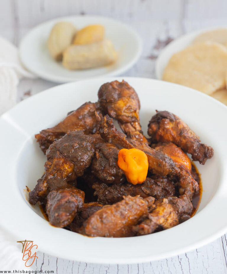 A bowl of stewed chicken wings in a white bowl with a plate of boiled plantains in the background.