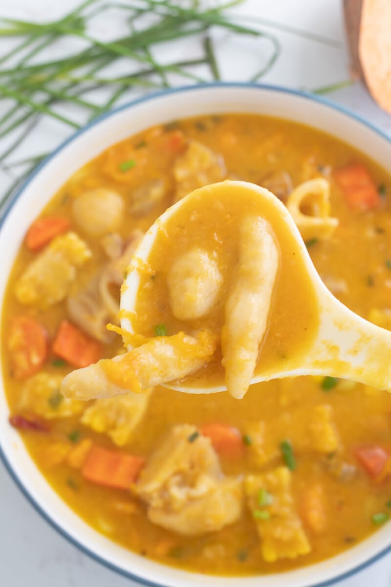 A picture of a spoon of dumplings over a pot of Caribbean cow heel soup.