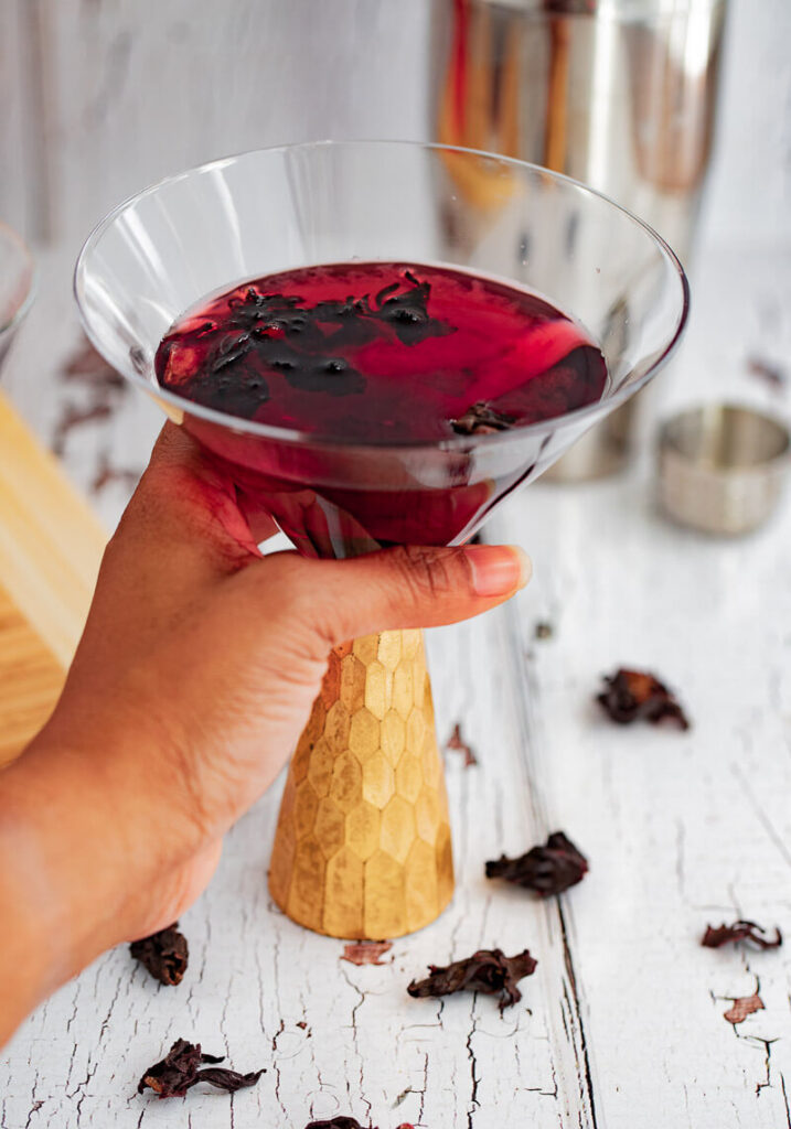 A hand picking up a glass of martini with a gold base.
