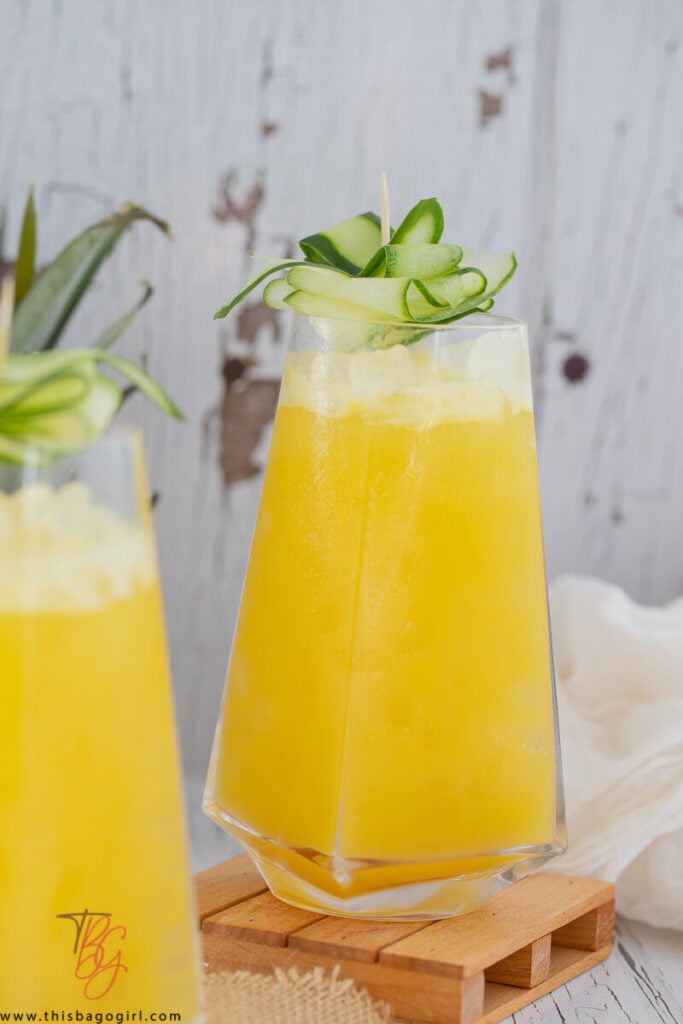 Close up picture of a glass of pineapple and cucumber juice with strips of cucumber on top for garnish.