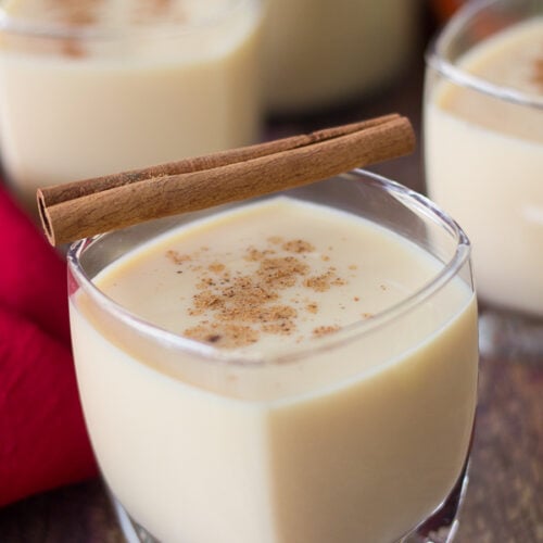 Glasses of ponche de creme with a cinnamon stick on top with a red napkin.