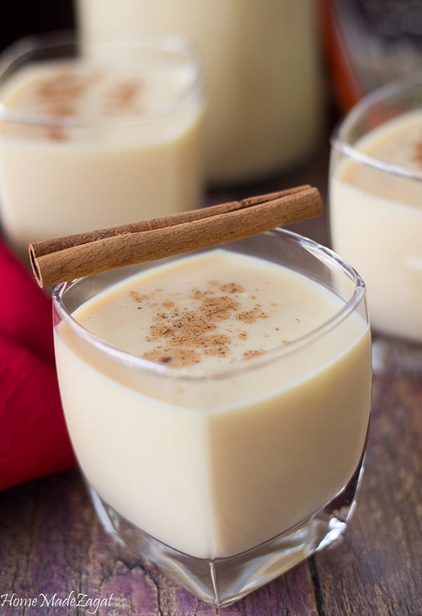 Glasses of ponche de creme with a cinnamon stick on top with a red napkin.