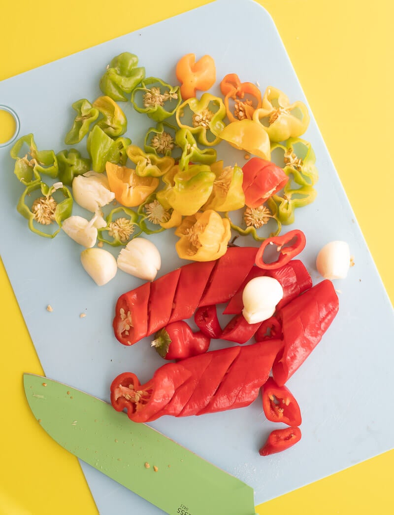 Chopped up peppers and garlic on a blue cutting board with a green background.