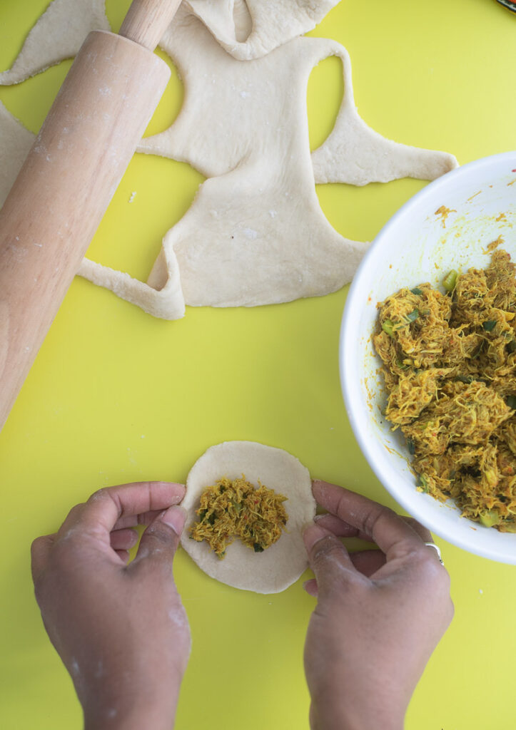 Two hands taking cooked curry crab and folding the dumplings closed.