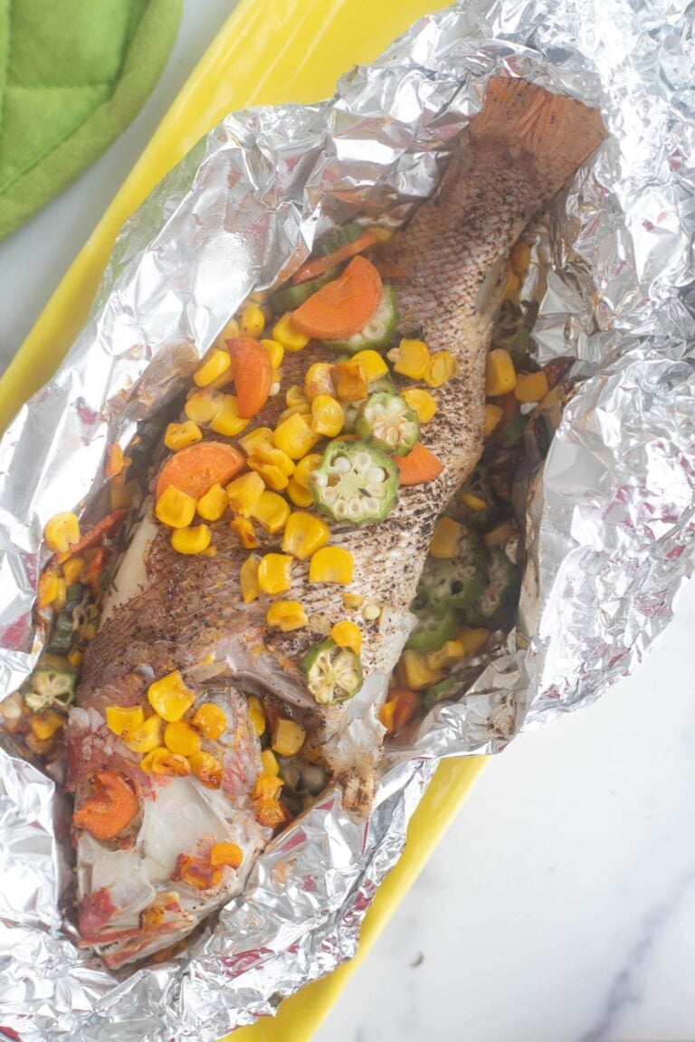 Whole snapper stuffed with aromatics in foil on a yellow plate.
