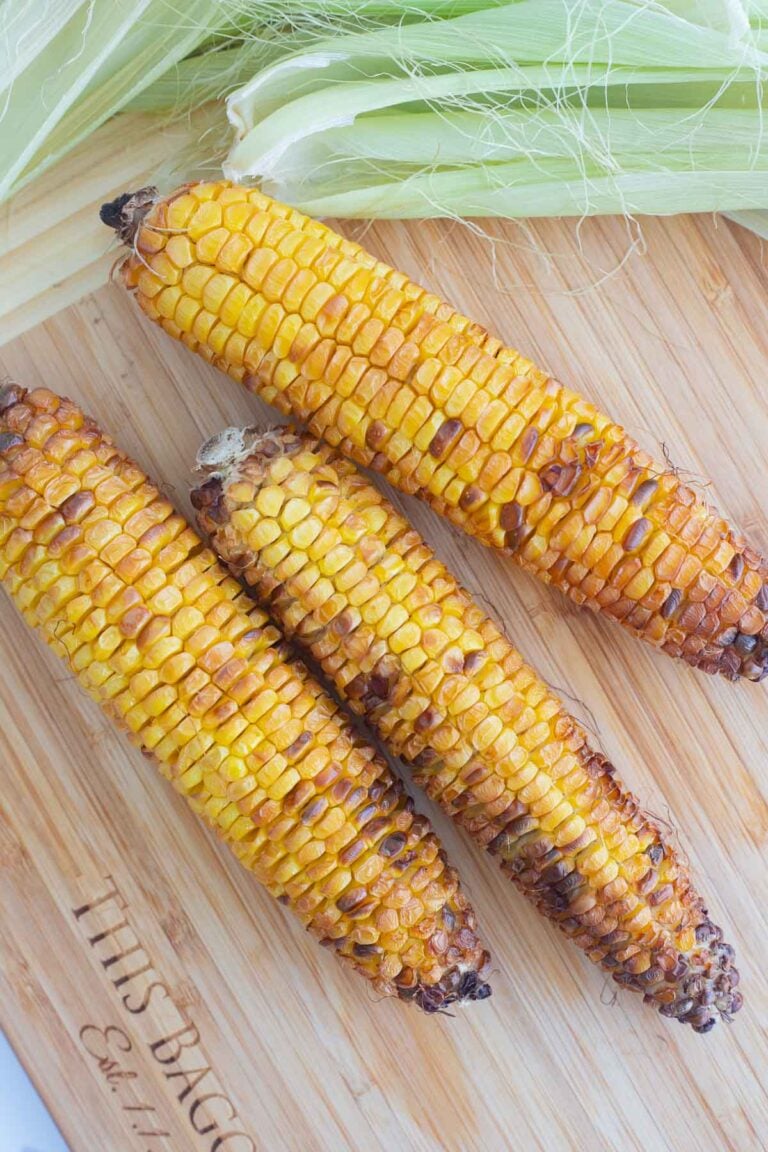 Picture of three ears of corn with grilled edges on a brown cutting board.