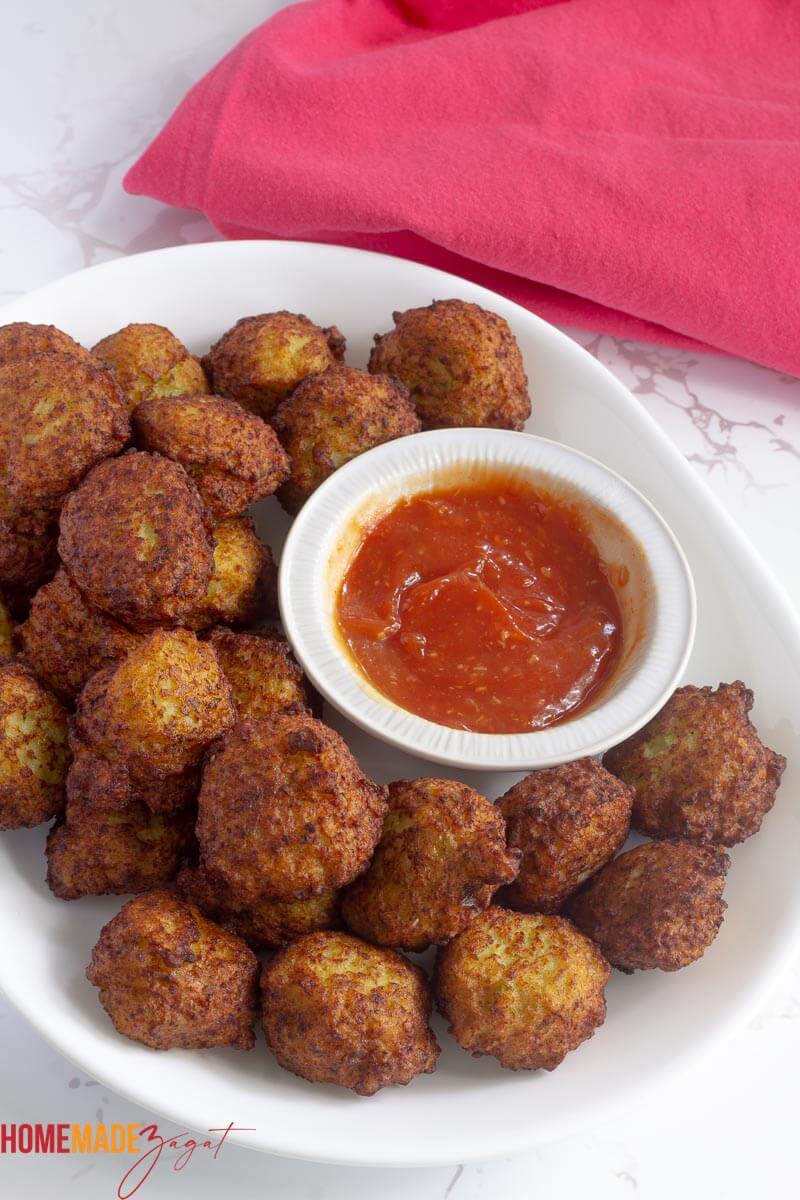 Golden fried conch fritters on a white plate with a bowl of red dipping sauce