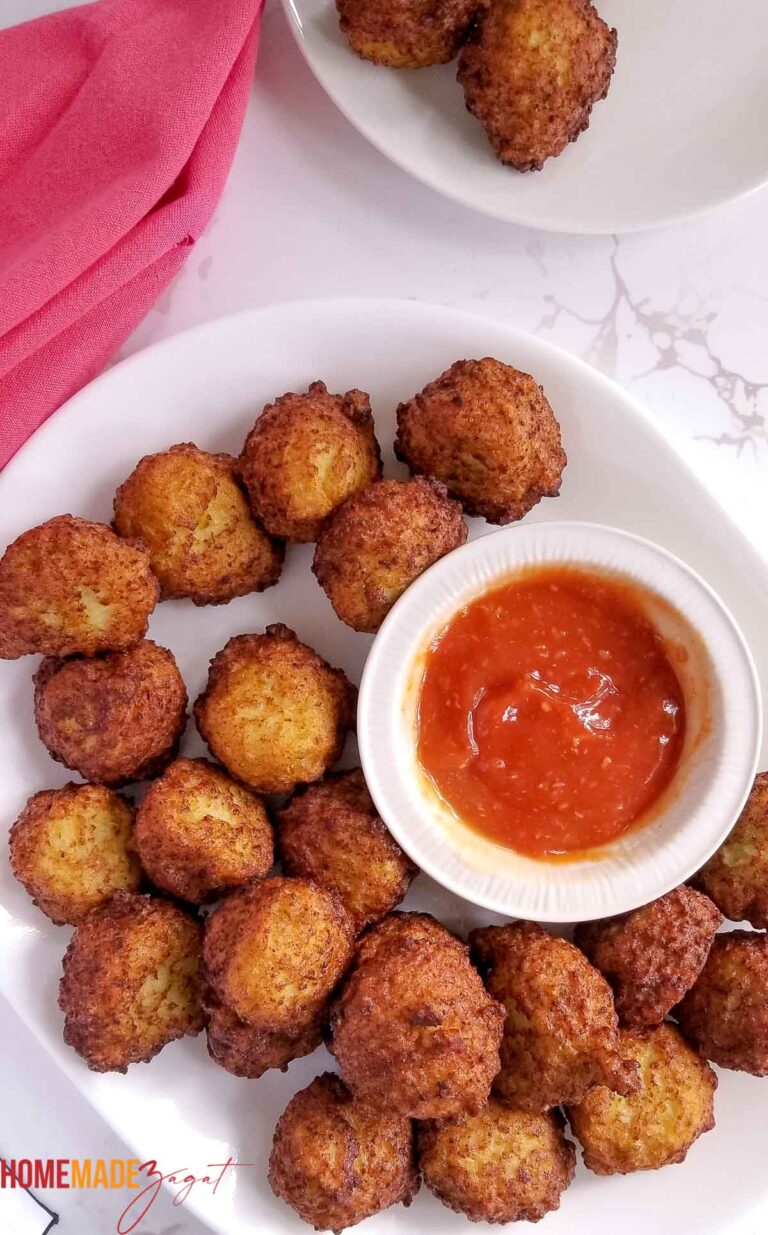 A plate of golden fried Bahamian conch fritters with a bowl of red dipping sauce