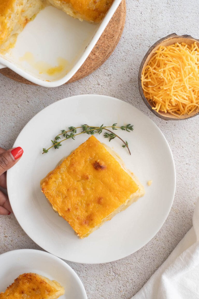 Slice of baked potato pie on a white plate with sprigs of fresh thyme for garnish.