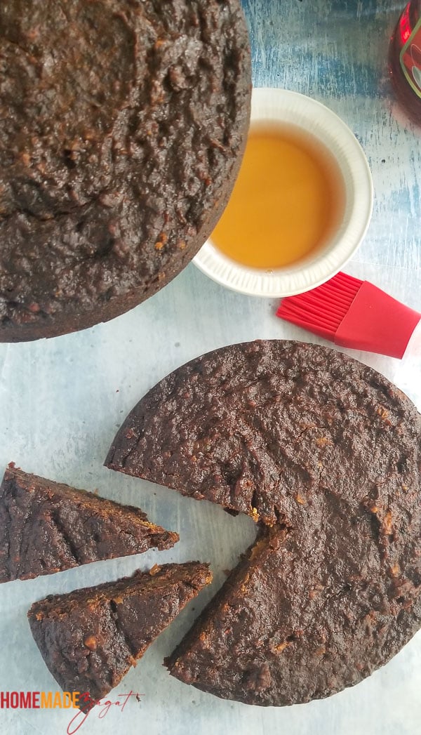Top view of 2 cassava black cakes and some rum in a white bowl to base. One has 2 slices