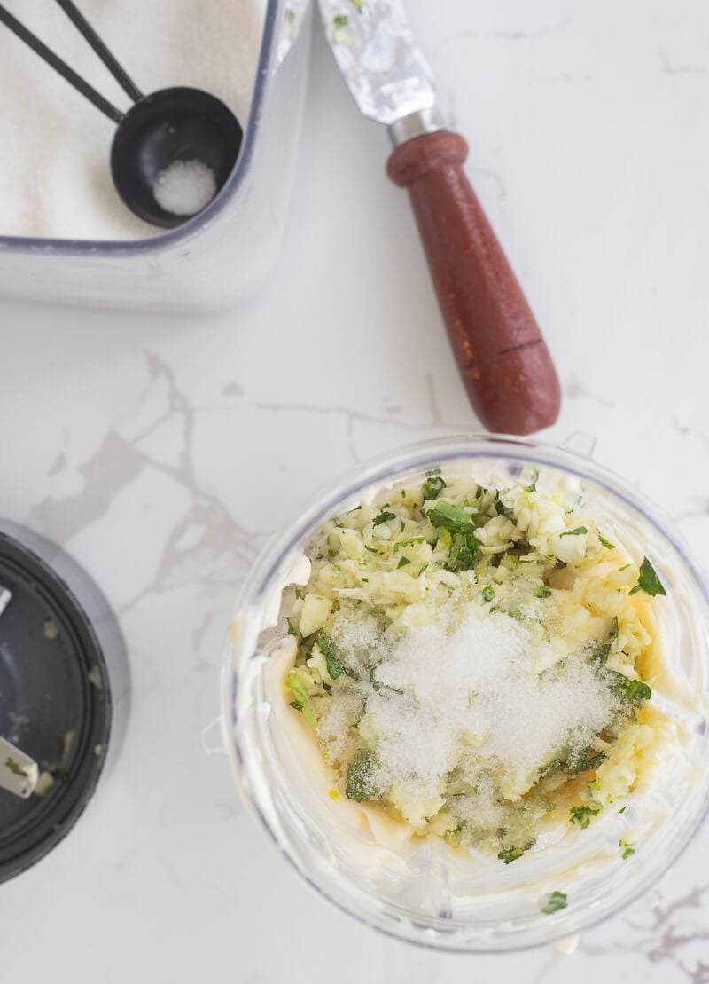 The blender bowl of crushed garlic and chadon beni, along with sugar and mayonnaise to be blended for garlic sauce.