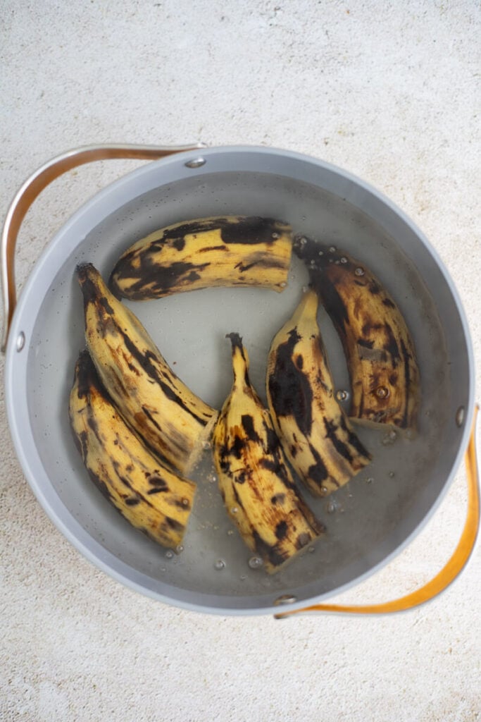 Plantains in a large pot of boiling water on a cream counter.