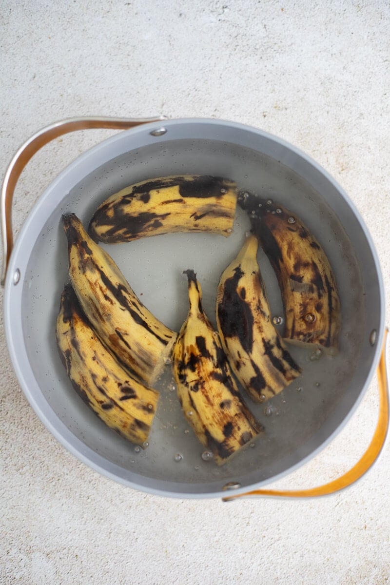 Plantains in a large pot of boiling water on a cream counter.